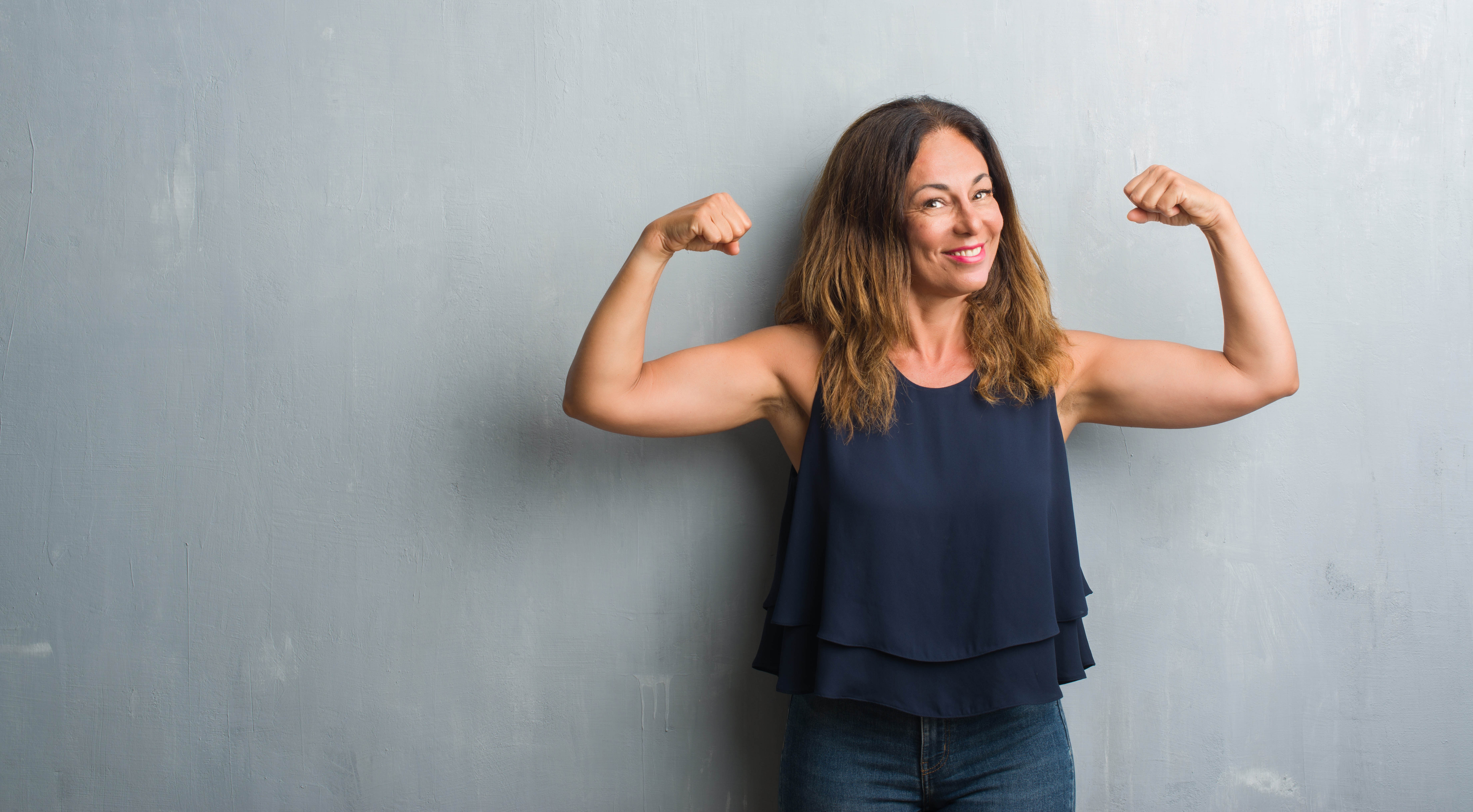 Middle aged fit woman smiling at the camera and flexing her arms